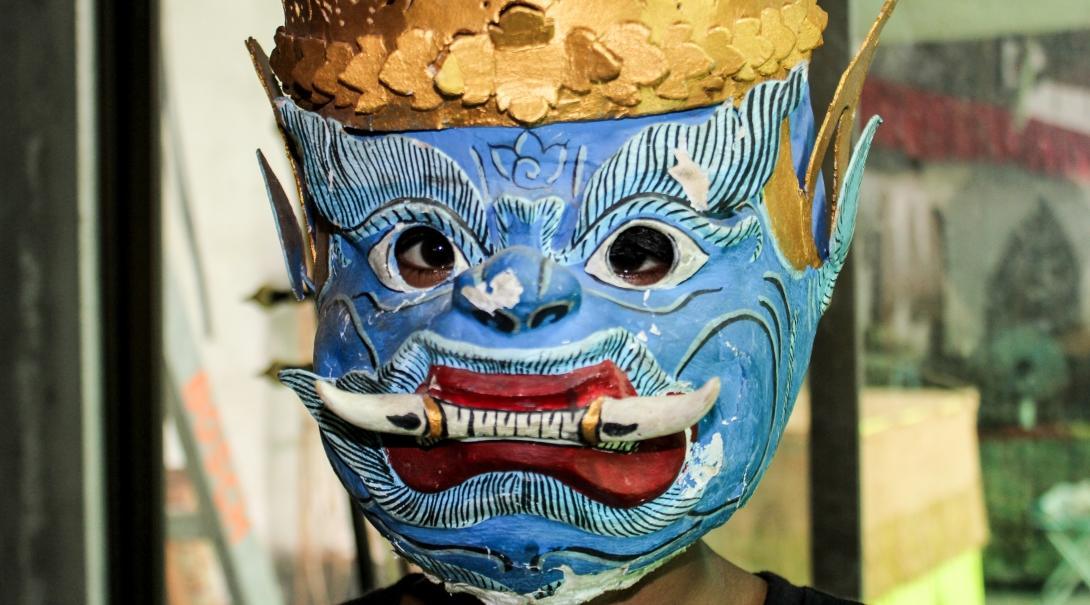 A senior Projects Abroad volunteer wears a traditional mask as part of the Khmer cultural experience in Cambodia. A volunteer over 50 learning about the Khmer culture in Cambodia, wears a traditional mask.